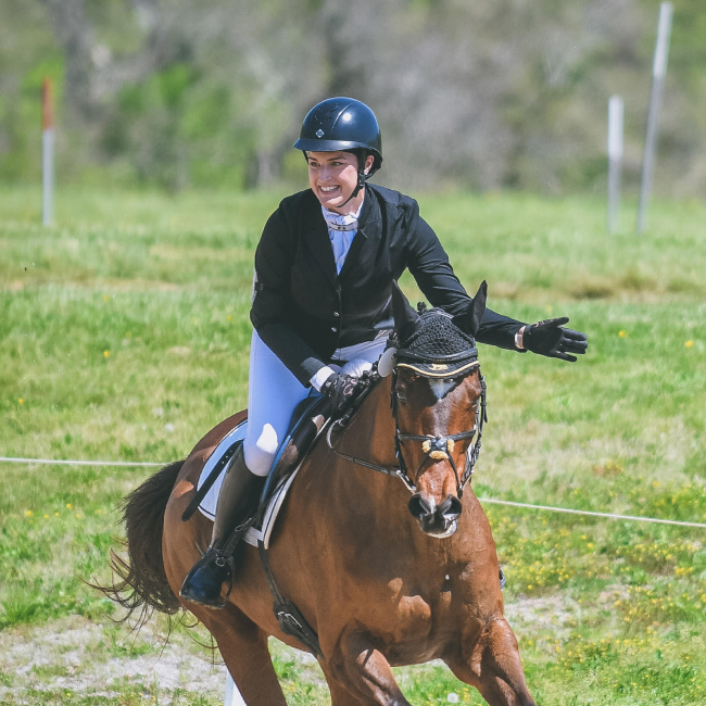 Megan Ferryman riding a brown horse while wearing a helmet and formal equestrian attire.